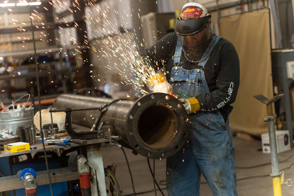 Welder working on a large pipe in a fabrication shop with sparks flying. Welder working on a large pipe in a fabrication shop with sparks flying.